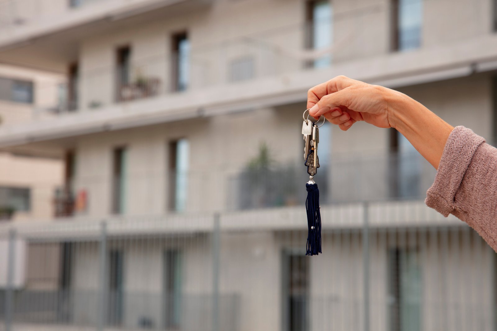 Imagén de una mano mostrando unas llaves de una viviendo, con edificio de fondo.